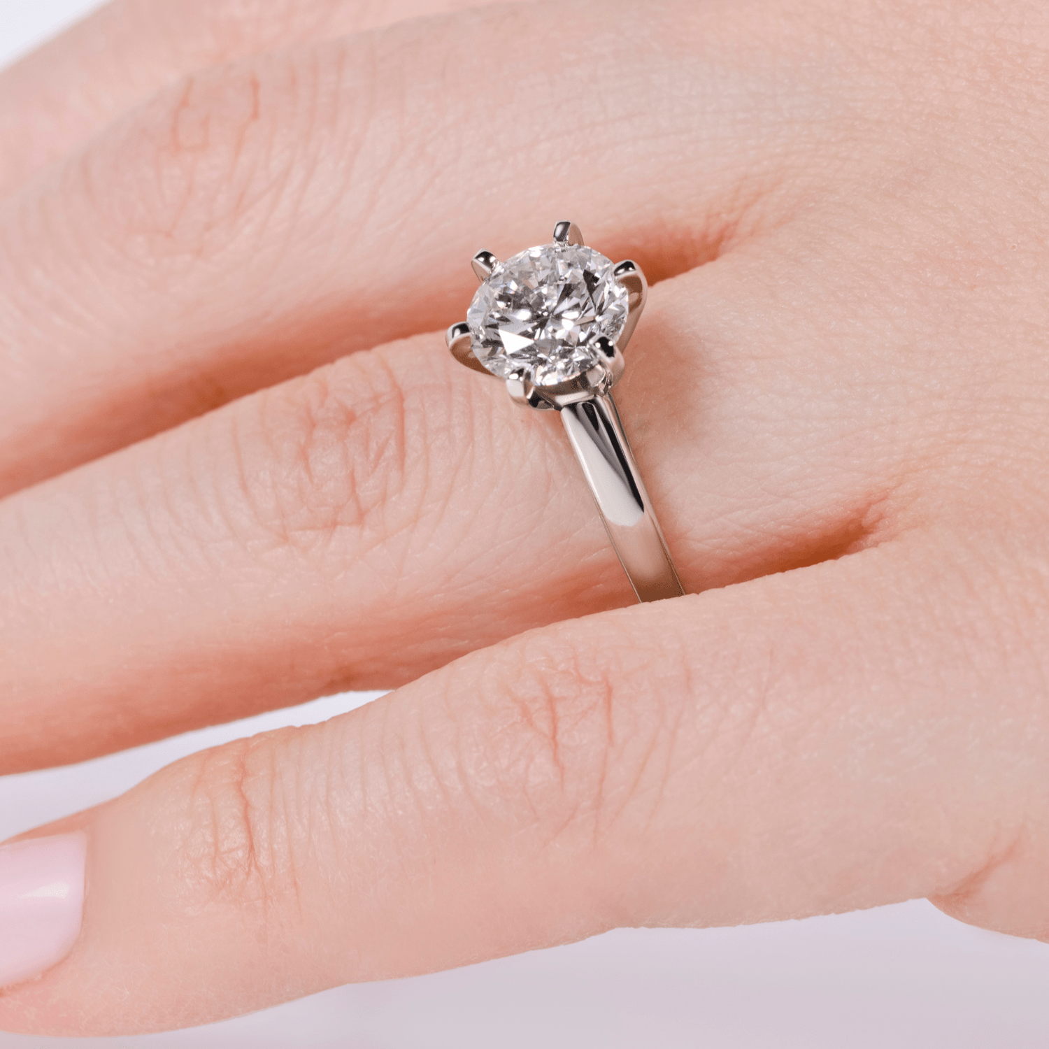 Close-up of a hand wearing a solitaire diamond engagement ring with a round brilliant center stone on a simple metal band.