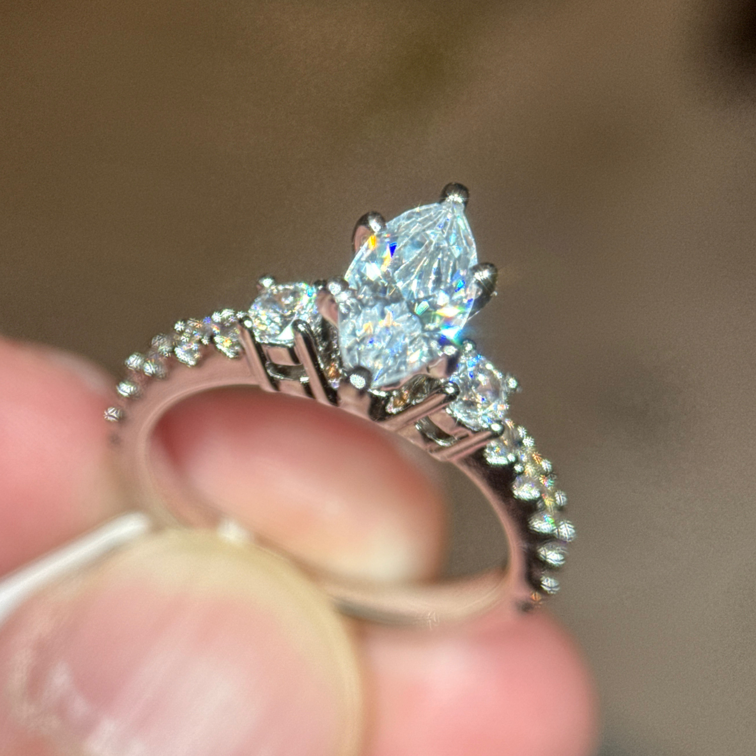 A close-up of a hand holding a marquise-cut diamond engagement ring with a sparkling center stone and a band lined with small round diamonds.